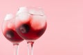 Summer fresh red cocktails in two wineglasses with blueberry, ice cubes on white wood table and pastel pink wall, copy space.