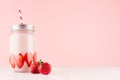 Summer fresh strawberry milkshake in jar with bright fruit, silver cap, red striped straw on elegance pink background, copy space.