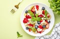 Summer fruit and berry salad with feta cheese, fresh strawberries, blueberries, banana, kiwi, orange and mint, green background, Royalty Free Stock Photo