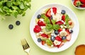 Summer fruit and berry salad with feta cheese, fresh strawberries, blueberries, banana, kiwi, orange and mint, green background, Royalty Free Stock Photo
