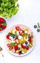 Summer fruit and berry salad with fresh strawberries, blueberries, banana, cottage cheese and mint on white table background, top Royalty Free Stock Photo