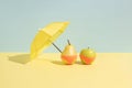 Summer fruit concept. Wet apple and a pear in monokini next to an umbrella isolated on a blue and yellow background. Royalty Free Stock Photo