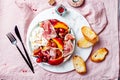 Summer fruit salad with burrata, peaches, figs, grapes, jamon or prosciutto and toasted bread on pink linen tablecloth.