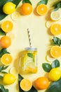 Summer fruits water with lemon, orange, mint and ice in mason jar on yellow. Tropical concept.