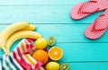 Summer fun time. Fruits on blue wooden background. Orange, lemon, kiwi, banana fruit in bag and flip flops on the floor. Top view