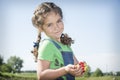 In summer, in the garden, a small curly girl holds a strawberry