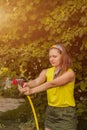 Summer garden, watering - beautiful girl watering roses with garden hose in the garden