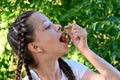 in the summer garden young cute girl with pigtails in white T-shirt brings one ripe cherry berry to her mouth.