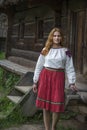 In summer, a girl in an authentic Ukrainian national costume poses against the backdrop of a hut in the Pirogovo Museum