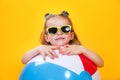 Summer girl wearing sunglasses with ball laughing on yellow background Royalty Free Stock Photo