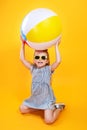 Summer girl wearing sunglasses holding ball laughing on yellow background Royalty Free Stock Photo