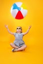 Summer girl wearing sunglasses playing with ball on yellow background Royalty Free Stock Photo