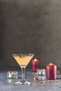Summer grapefruit martini cocktail with dried roses flowers and petals, surrounded candles on dark gray table surface