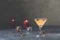 Summer grapefruit martini cocktail with dried roses flowers and petals, surrounded candles on dark gray table surface