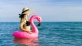 Summer hat beach. Happy young sexy girl in bikini swimsuit, sunglasses and straw hat with pink inflatable flamingo in blue sea Royalty Free Stock Photo