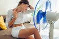 Summer heat. Air conditioning. Young woman cooling down feeling hot sitting on couch by ventilator at home