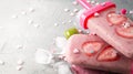 Summer heat: refreshing pink fruit ice with strawberry pieces surrounded by transparent and green ice cubes on a gray table.