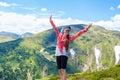 Summer hiking in the mountains. Young tourist girl with long hair in a cap with hands up on the top of the mountains Royalty Free Stock Photo