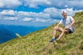 Summer hiking in the mountains. Young tourist man in a cap with hands up on the top of the mountains admires the nature Royalty Free Stock Photo