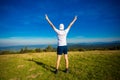 Summer hiking in mountains. Young tourist man in cap with hands up on top of mountains admires nature Royalty Free Stock Photo