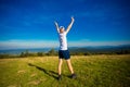 Summer hiking in mountains. Young tourist man in cap with hands up on top of mountains admires nature Royalty Free Stock Photo