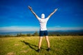 Summer hiking in mountains. Young tourist man in cap with hands up on top of mountains admires nature. Royalty Free Stock Photo