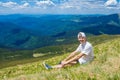 Summer hiking in the mountains. Young tourist man in a cap with hands up on the top of the mountains admires the nature Royalty Free Stock Photo