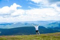 Summer hiking in the mountains. Young tourist man in a cap with hands up on the top of the mountains admires the nature Royalty Free Stock Photo