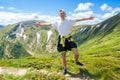 Summer hiking in the mountains. Young tourist man in a cap with hands up on the top of the mountains admires the nature Royalty Free Stock Photo