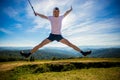 Summer hiking in mountains. Young tourist man in cap with hands up on top of mountains admires nature Royalty Free Stock Photo