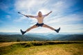 Summer hiking in mountains. Young tourist man in cap with hands up on top of mountains admires nature Royalty Free Stock Photo