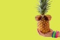 Summer and Holiday concept.Hipster hand holding Pineapple Fashion Accessories and Fruits on yellow background
