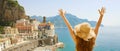 Summer holiday in Italy. Panoramic back view of young woman with straw hat with raised arms looking at Atrani village, Amalfi