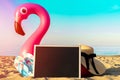 Summer holiday poster. Funny pink toy flamingo with blackboard, slippers and hat for text on summer ocean nature beach background Royalty Free Stock Photo