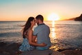 Summer holiday. Woman and man posing against the sea, sitting on the rocks in an embrace. Rear view. Sunset Royalty Free Stock Photo