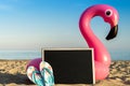 Summer holidays background. Pink inflatable flamingo with black desk, slippers for text on summer sea beach background Royalty Free Stock Photo