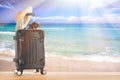 Summer holidays concept. Suitcase baggage with straw hat and retro camera against sandy tropical beach and turquoise water ocean. Royalty Free Stock Photo