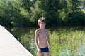 Happy boy 11 years old goes swimming on a wooden pier, on the background of the shore and the lake on a summer sunny day Royalty Free Stock Photo