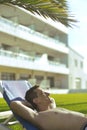 Summer holidays. Young man sunbathing. In the background a palm tree. Vacation concept. Man freelancer lies on a blue lounger.