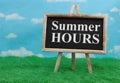 Summer Hours message on standing chalkboard on grass with sky