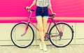 Summer image of legs of beautiful young woman in shorts posing with bicycle in the city on pink background Royalty Free Stock Photo