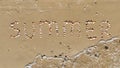 Summer inscription on the sand. The word summer laid out with shells on the sand and a sea wave. Letters made by Shells