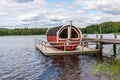 Summer lake nature landscape view of a traditional scandinavian water floating red wooden sauna spa next to a jetty. Royalty Free Stock Photo