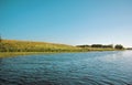 Summer lake near the field with green grass, the view from the boat on the water