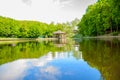 In the summer on the lake. Wooden house on the shore of the pond. Reflection of blue sky clouds in water.