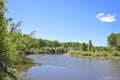 Summer landscape - A calm flat river among fields and birch groves under a blue sky.