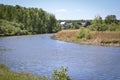 Summer landscape - a calm flat river among fields and birch groves under a blue sky. Village houses on the other side.