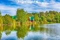 Summer landscape. Cozy wooden houses are hidden behind lush green trees on the shore of a beautiful lake on a warm summer evening Royalty Free Stock Photo