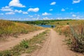 Summer landscape with dirt road to lake and blue sky with white clouds Royalty Free Stock Photo