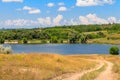 Summer landscape with dirt road to lake and blue sky with white clouds Royalty Free Stock Photo